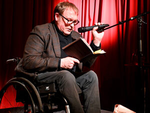 Mikkel Øyen i rullestol leser fra bok på scene