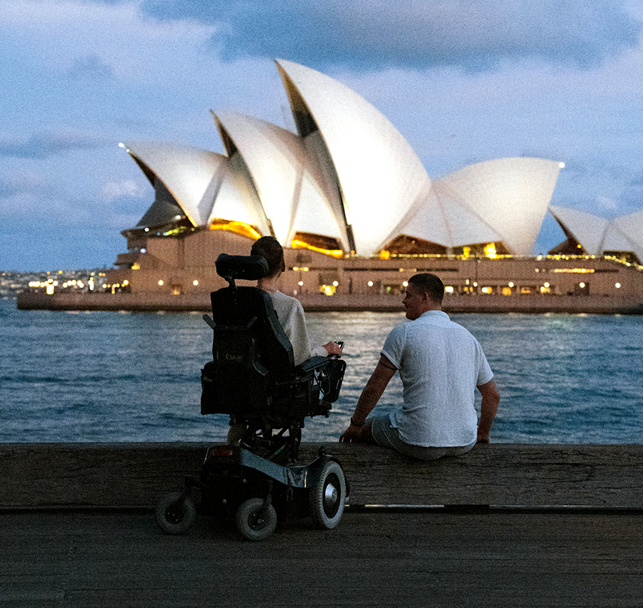 Daniel Maudal og assistent sitter i havna og ser over på Operahuset i Sydney.